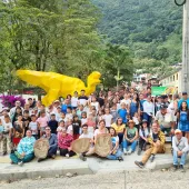 Large community group photo with families and children posing around large yellow sculpture in mountainous Colombian town setting