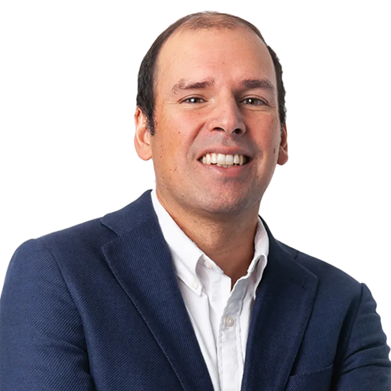 Professional headshot of a person wearing a navy blue blazer and white button-down shirt, photographed against a plain light background. The image is cropped from the chest up, with the subject facing the camera in a studio-style portrait.